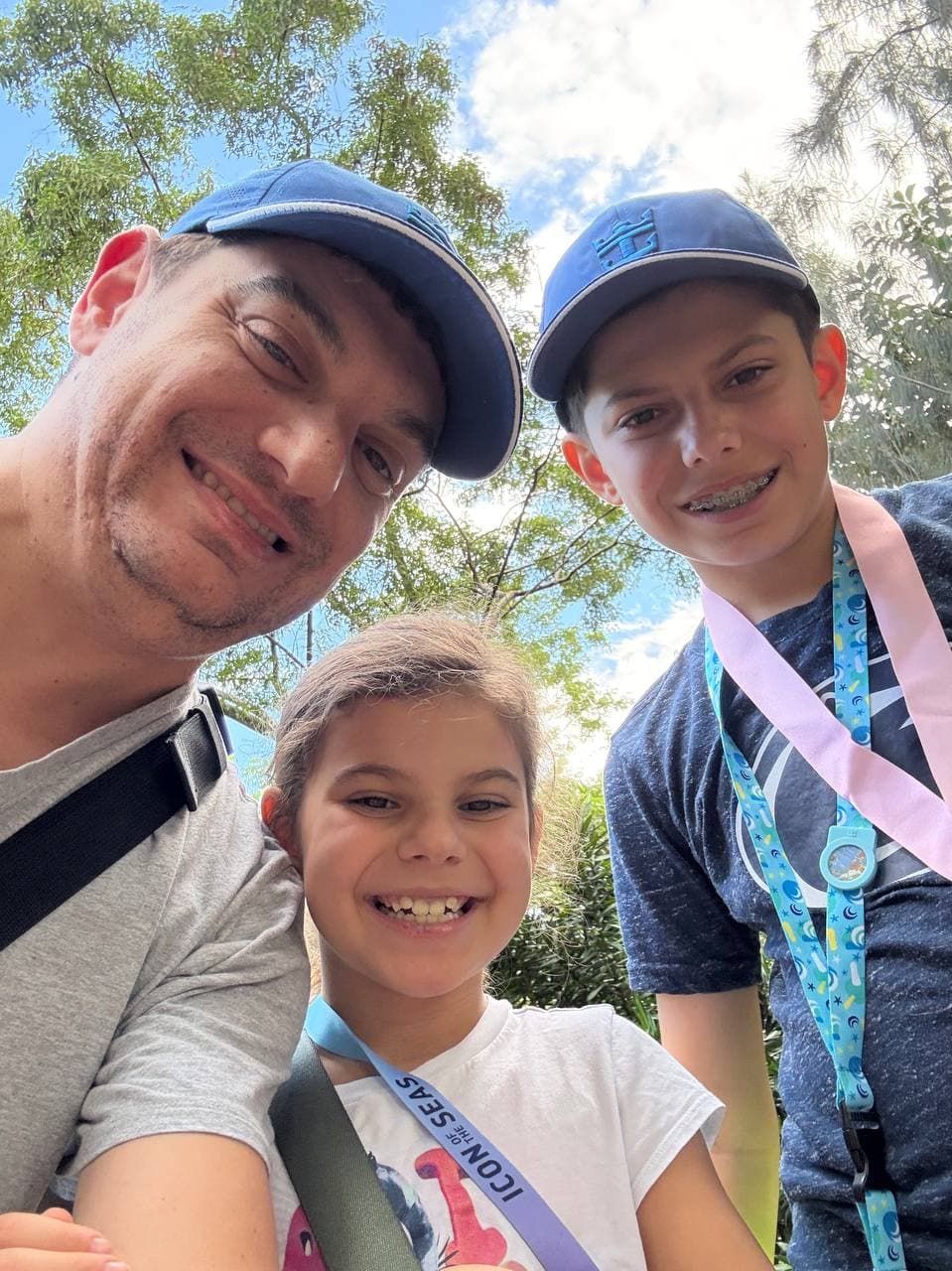 John, founder of Smart Dad Travel, outdoors with his two kids in baseball caps wearing a Royal Caribbean Icon of the Seas lanyard